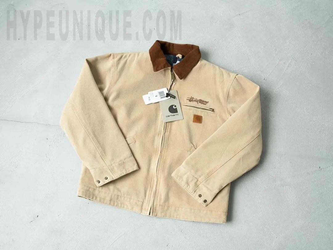 Carhartt x Stussy J97 Jacket Beige front view. Showing the Stussy logo on the left chest.