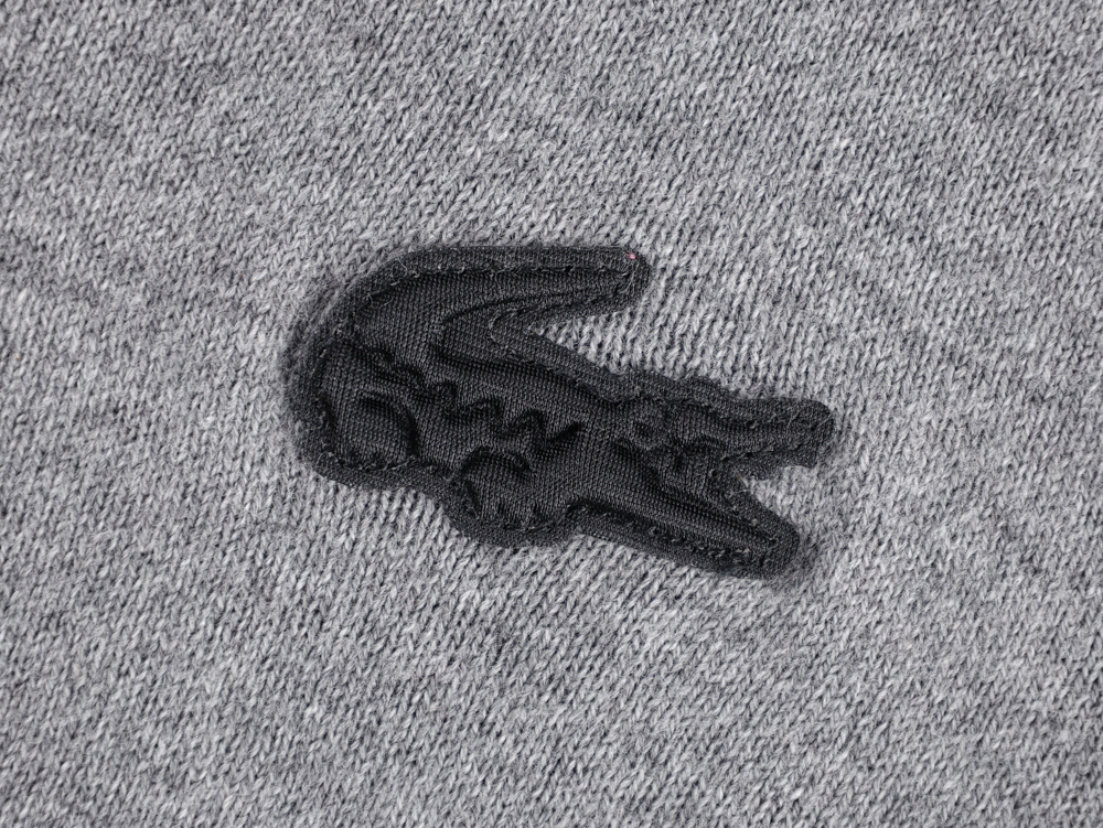Gray textured fabric with a black embroidered crocodile logo, featuring intricate stitching details and a subtly raised surface.