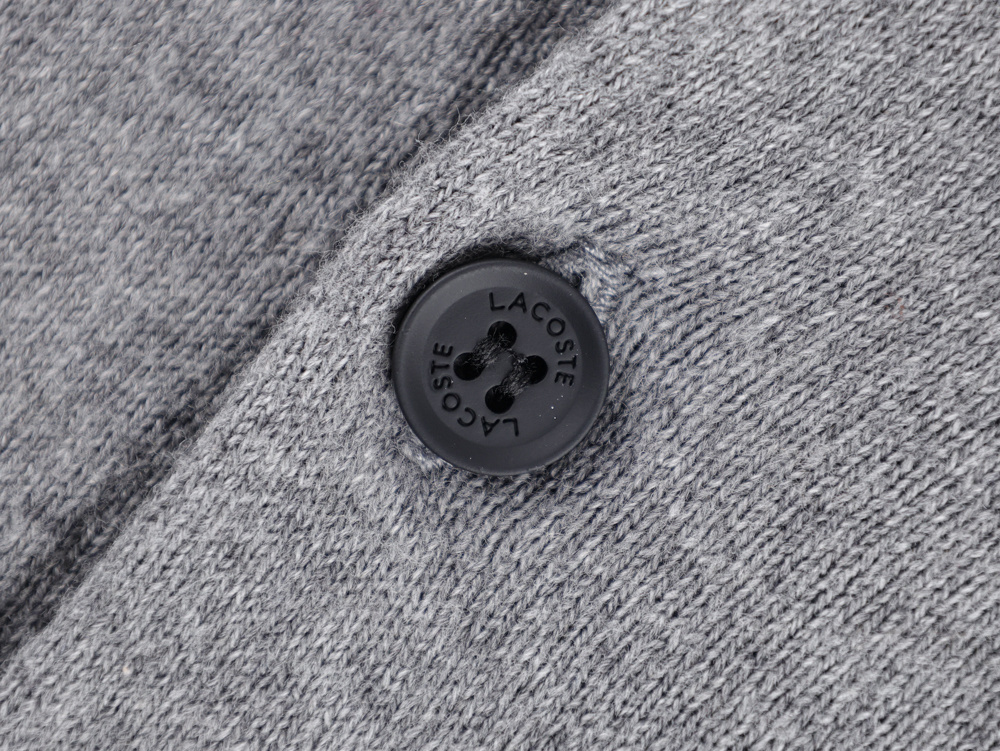Close-up of a grey polo shirt with textured fabric, featuring black buttons and emblem, and a labeled white tag.