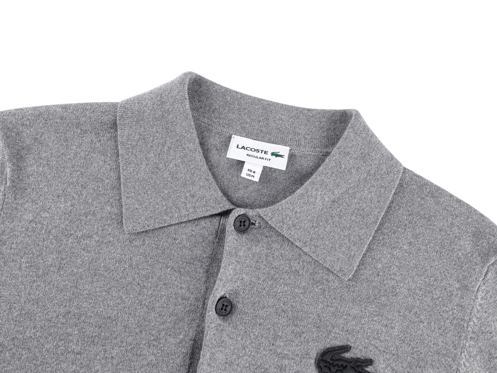 Gray knit polo shirt with black buttons, featuring a textured collar and embroidered logo. The fabric appears soft and fine.