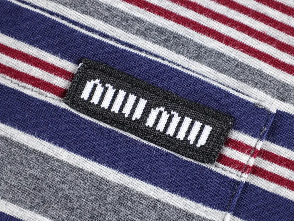 Striped fabric in red, gray, and navy with a black rectangular label featuring white text, stitched diagonally.