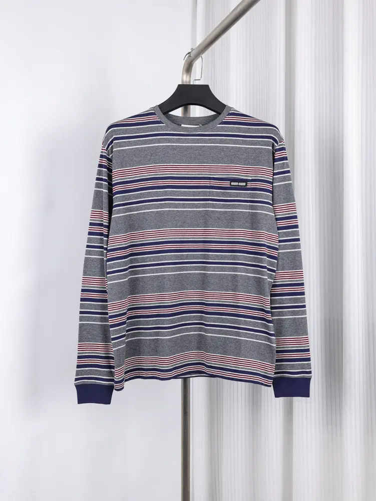 Gray long-sleeve shirt with horizontal blue, red, and white stripes, hanging on a black hanger against a white background.