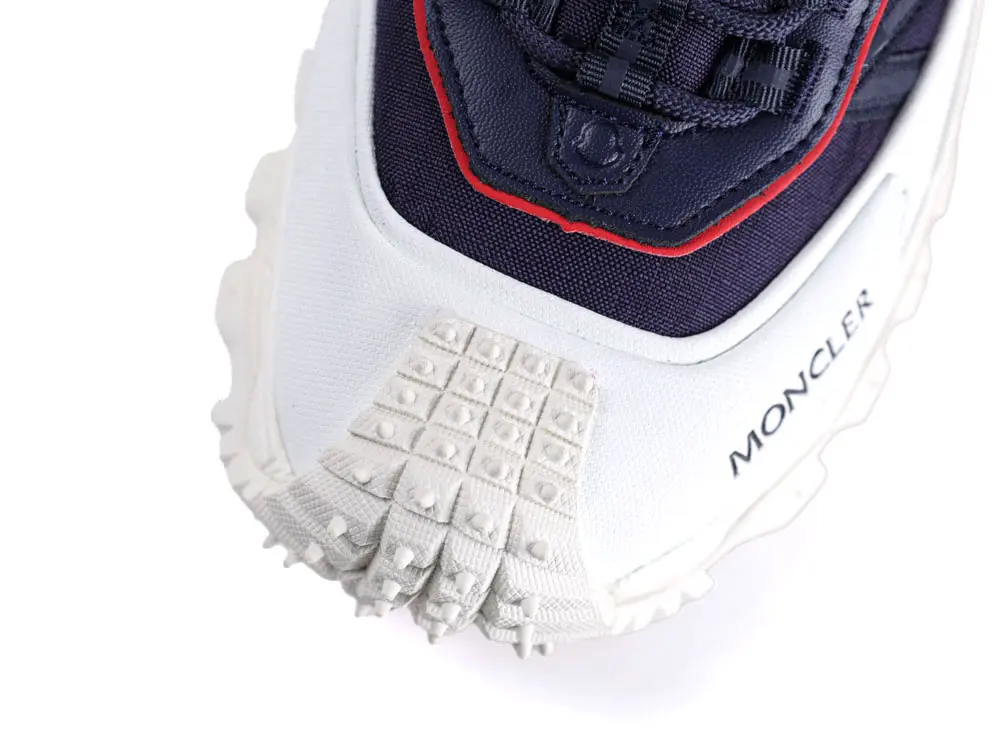 White and navy sneaker with red accents, textured rubber sole, Moncler branding visible.