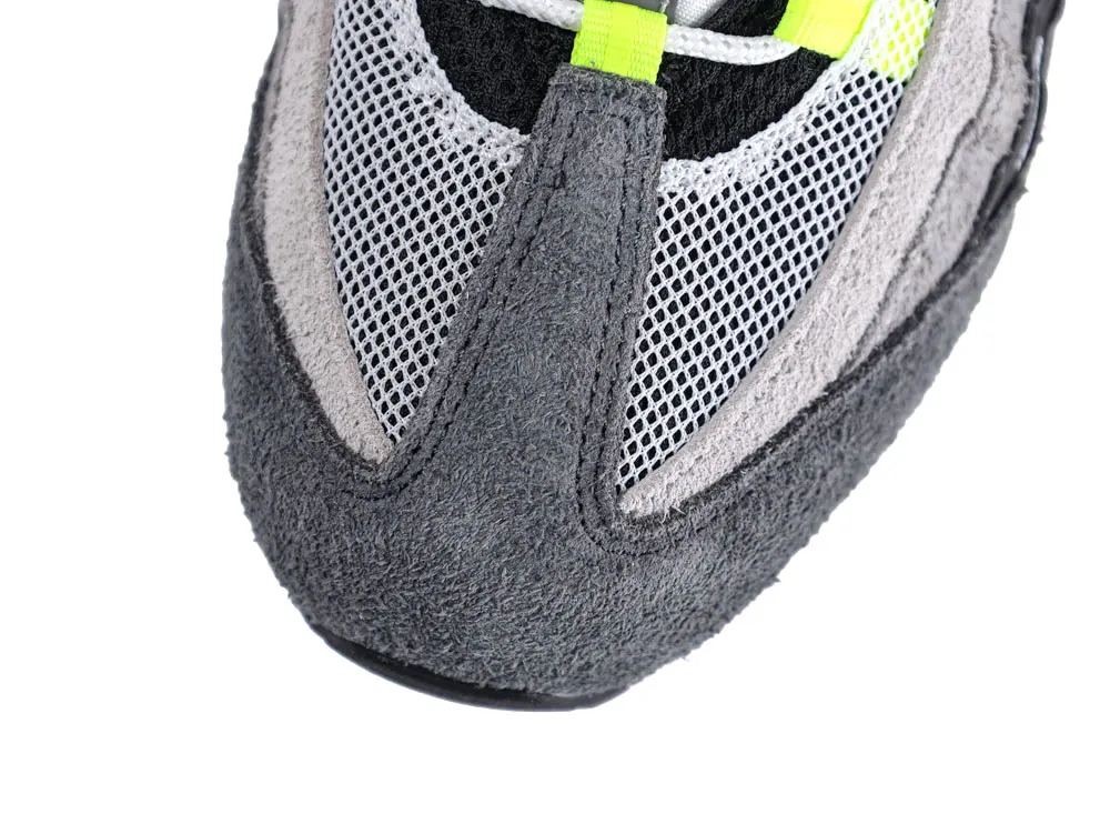 Close-up of a sneaker toe with gray suede and mesh, plus neon details.