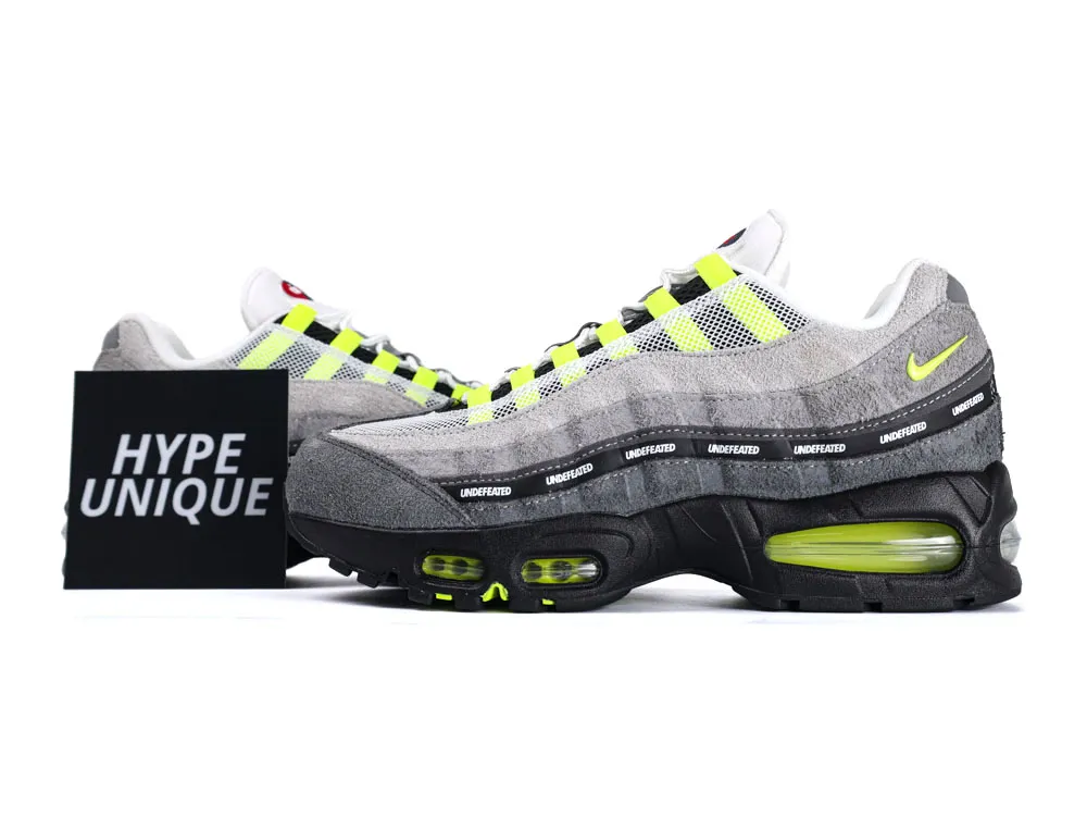 Gray and yellow suede sneakers with mesh upper and black sole displaying "Undefeated."