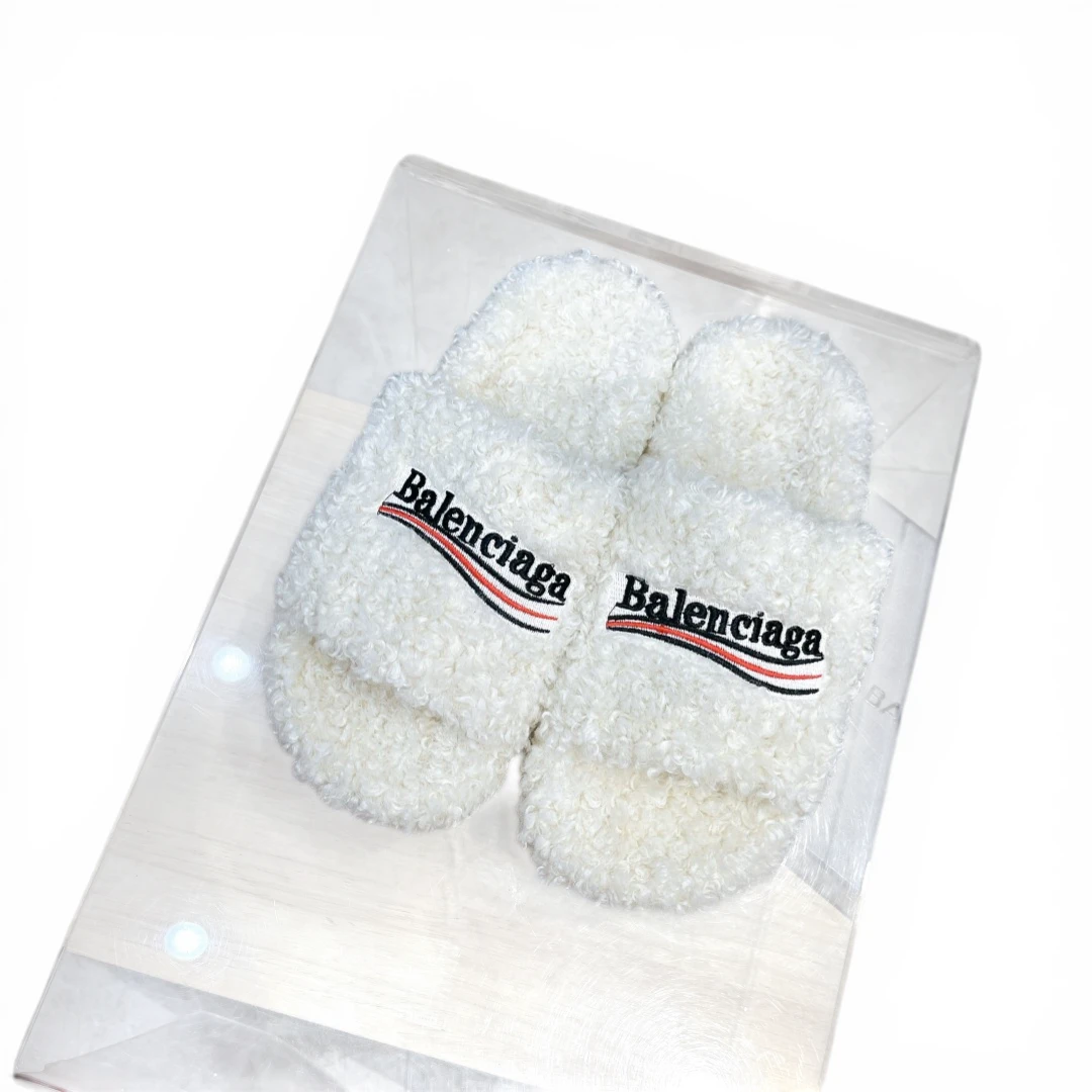 White fluffy slippers with embroidered logo on strap, made from soft material.