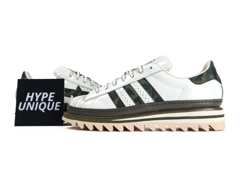 White leather sneaker with green camouflage accents and jagged sole.
