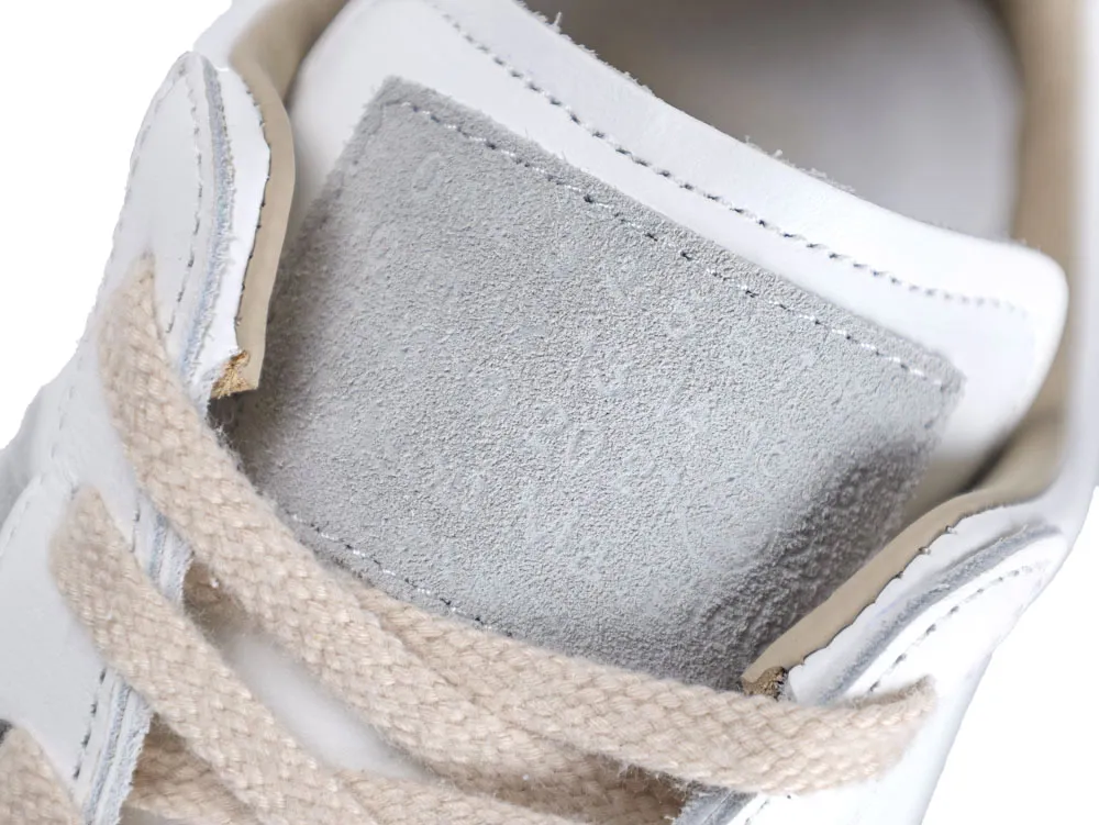 White leather shoe with gray suede tongue and beige fabric laces.