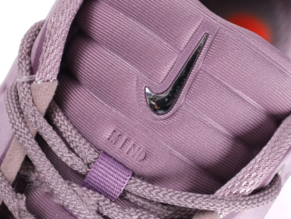 Close-up of a purple fabric shoe tongue with a metallic logo and laces.
