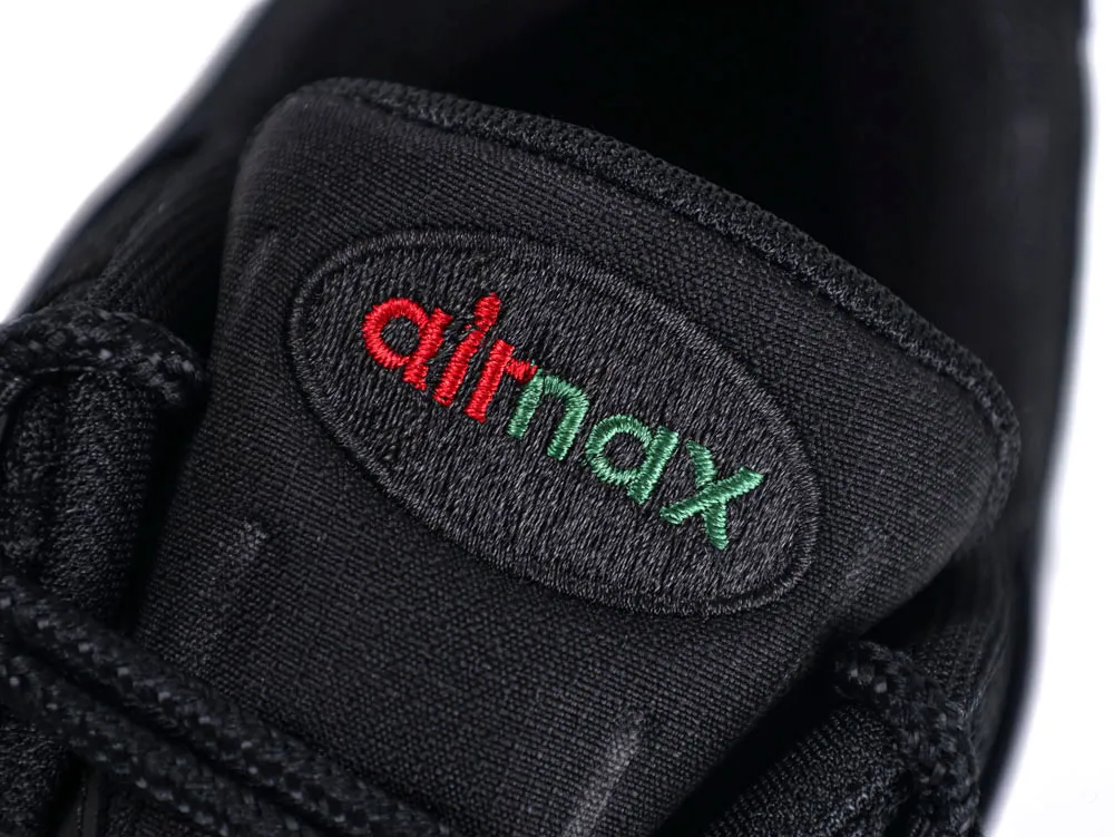 Close-up of black fabric shoe tongue with red and green embroidered logo.