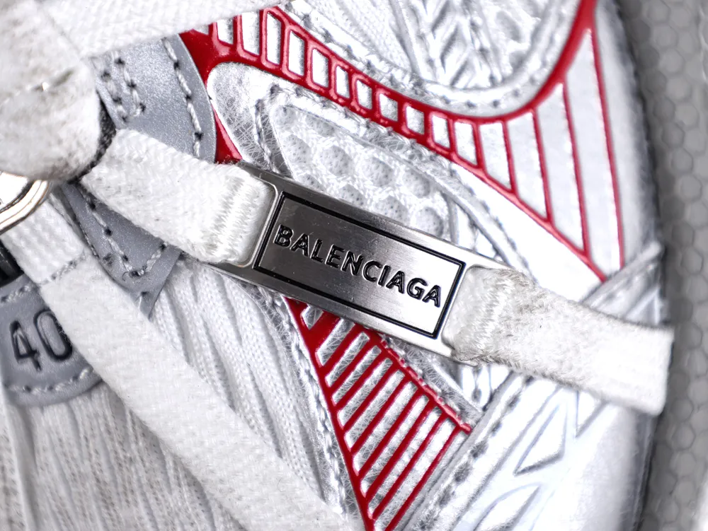 Close-up of silver and white sneaker with metal logo plate and red accents.