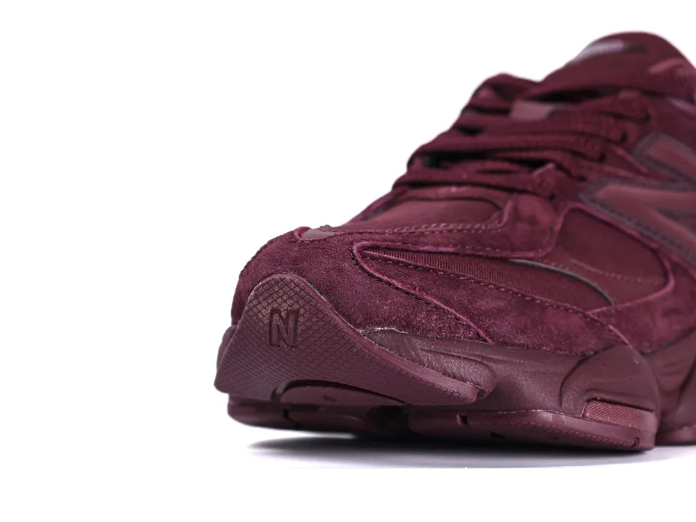 Close-up of a maroon suede sneaker's toe, showcasing detailed stitching and texture.