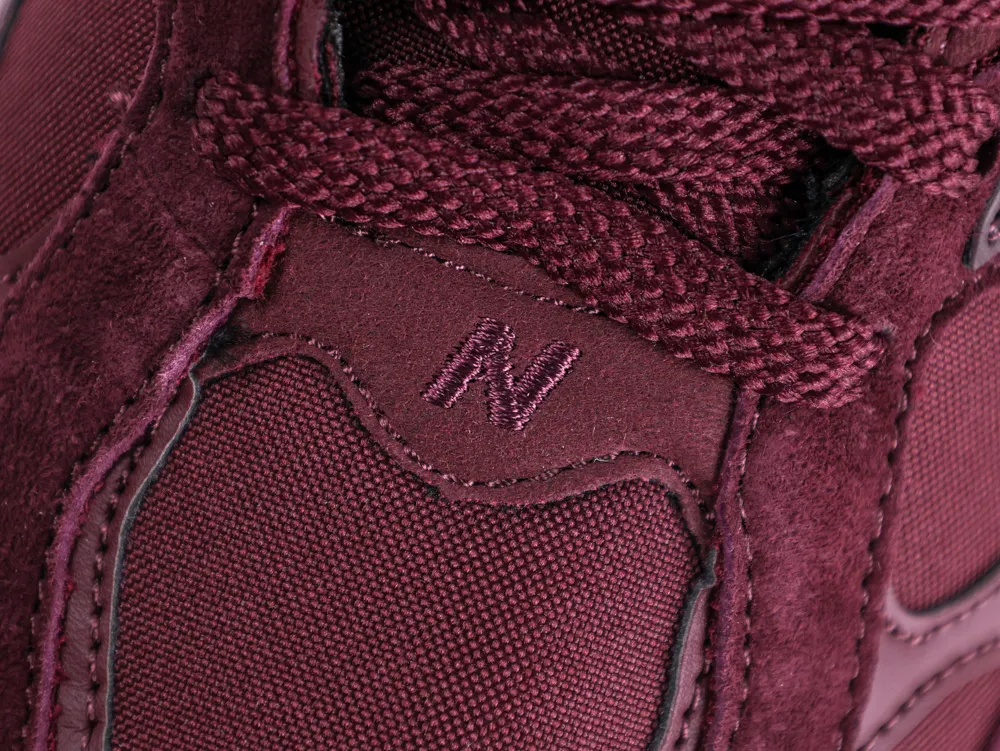 Close-up of a burgundy sneaker, showcasing fabric and suede material with laces.